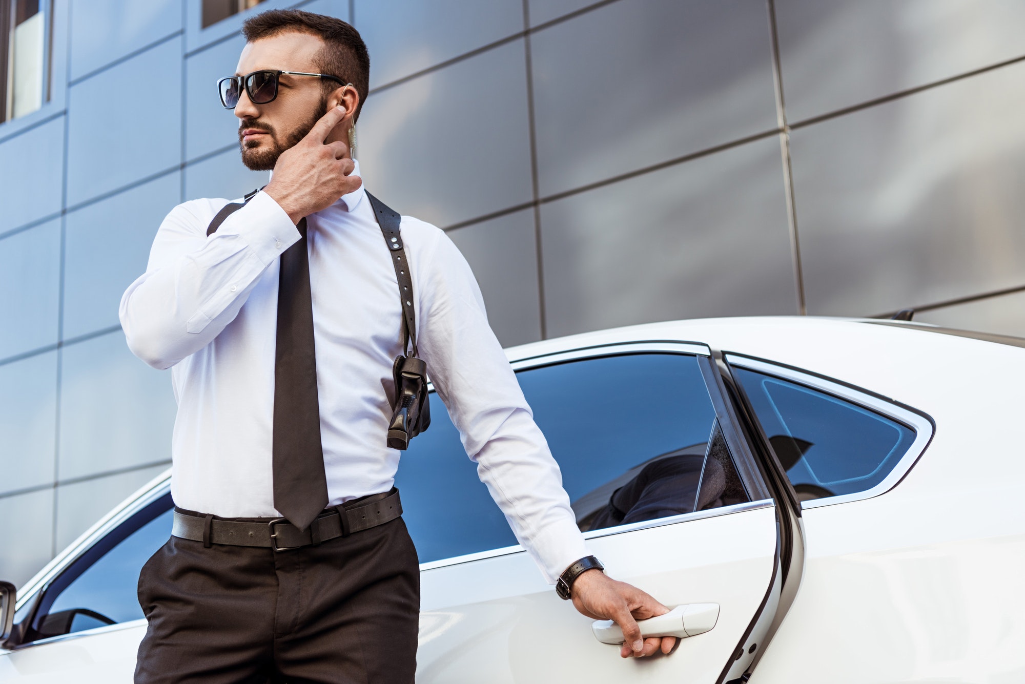 Guardia de seguridad AVSEC Handsome security guard listening message with security earpiece on street and opening car